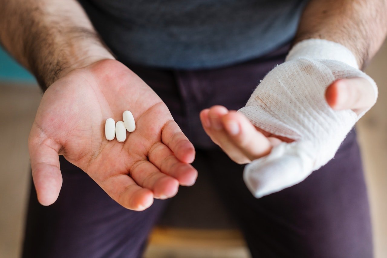 man with injured hand holding white pills