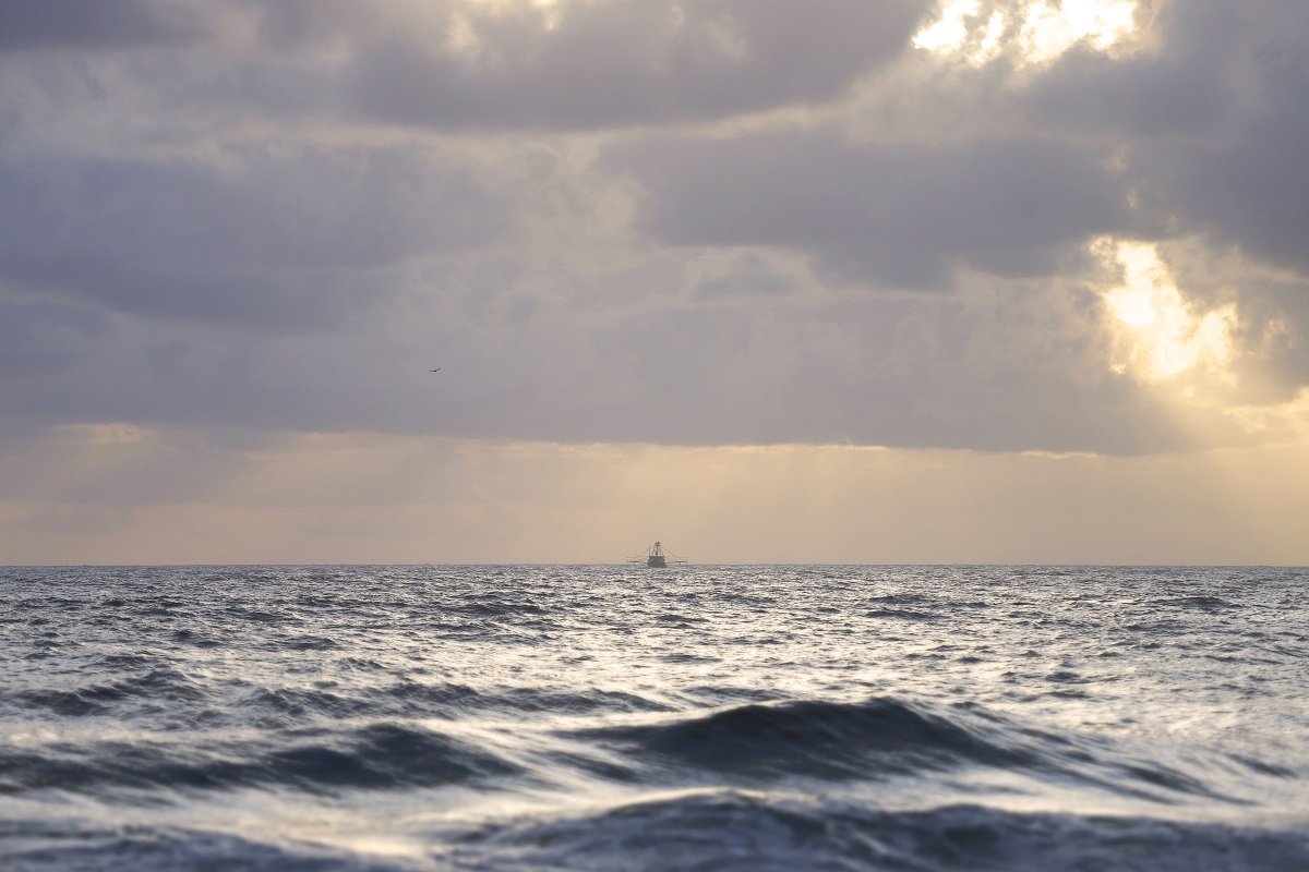 Fishing trawler sailing through rough seas at sunrise under stormy skies