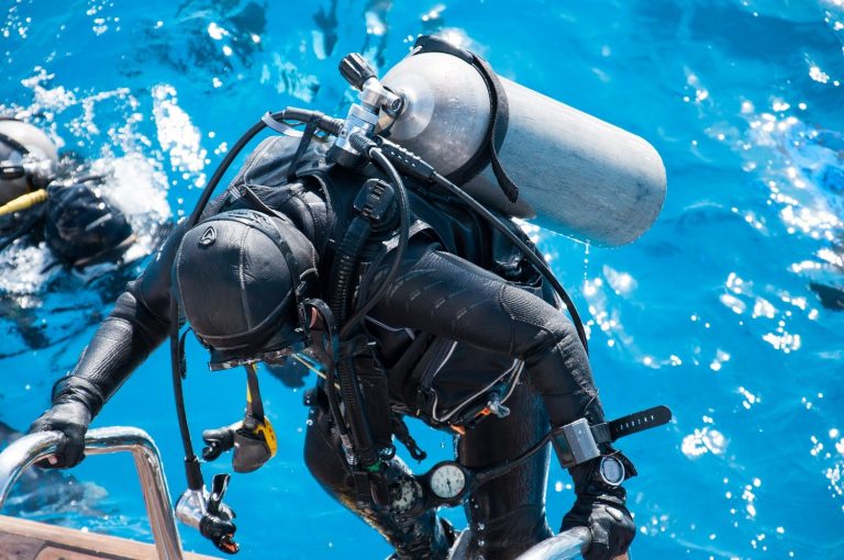 A woman in a wetsuit with a scuba gear rises to the deck of a yacht.