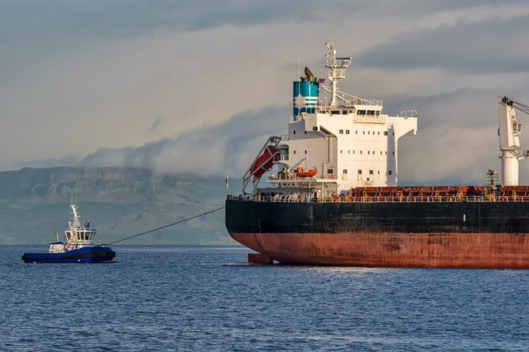 cargo ship coming into habour being towed by a tug boat