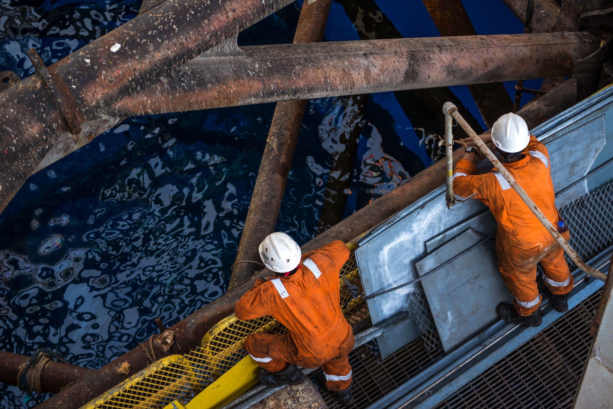 Two workers at jack up oil rig leg when checking everything in rig move operation