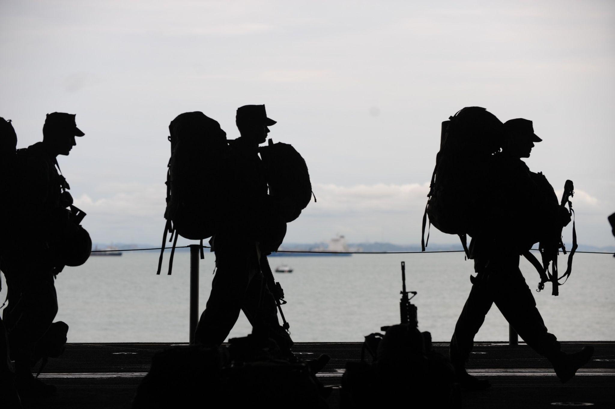 Silhouette of soldiers with backpack on a sunset dark background.