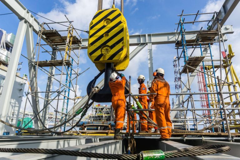 Offshore construction workers handling sling onto crane hook prior to heavy lifting on a construction barge at oil field