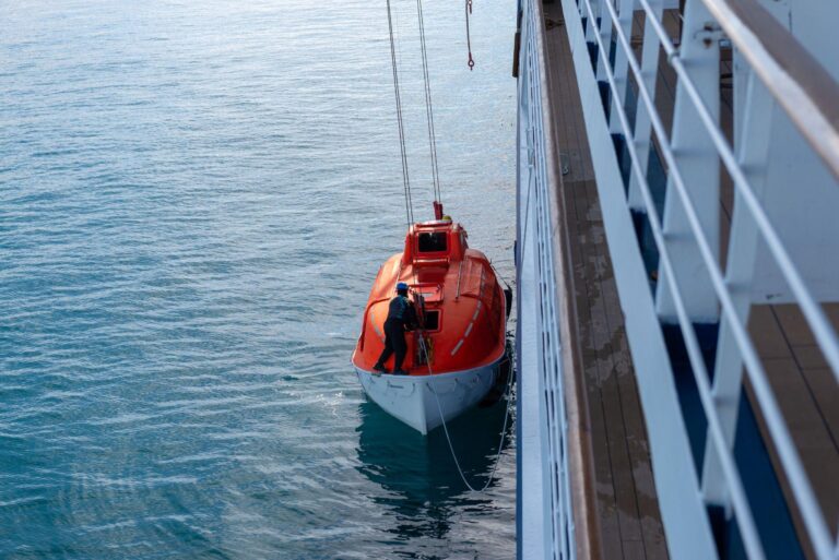 Lowering orange lifeboat to water in Arctic waters, Svalbard. Abandon ship drill.