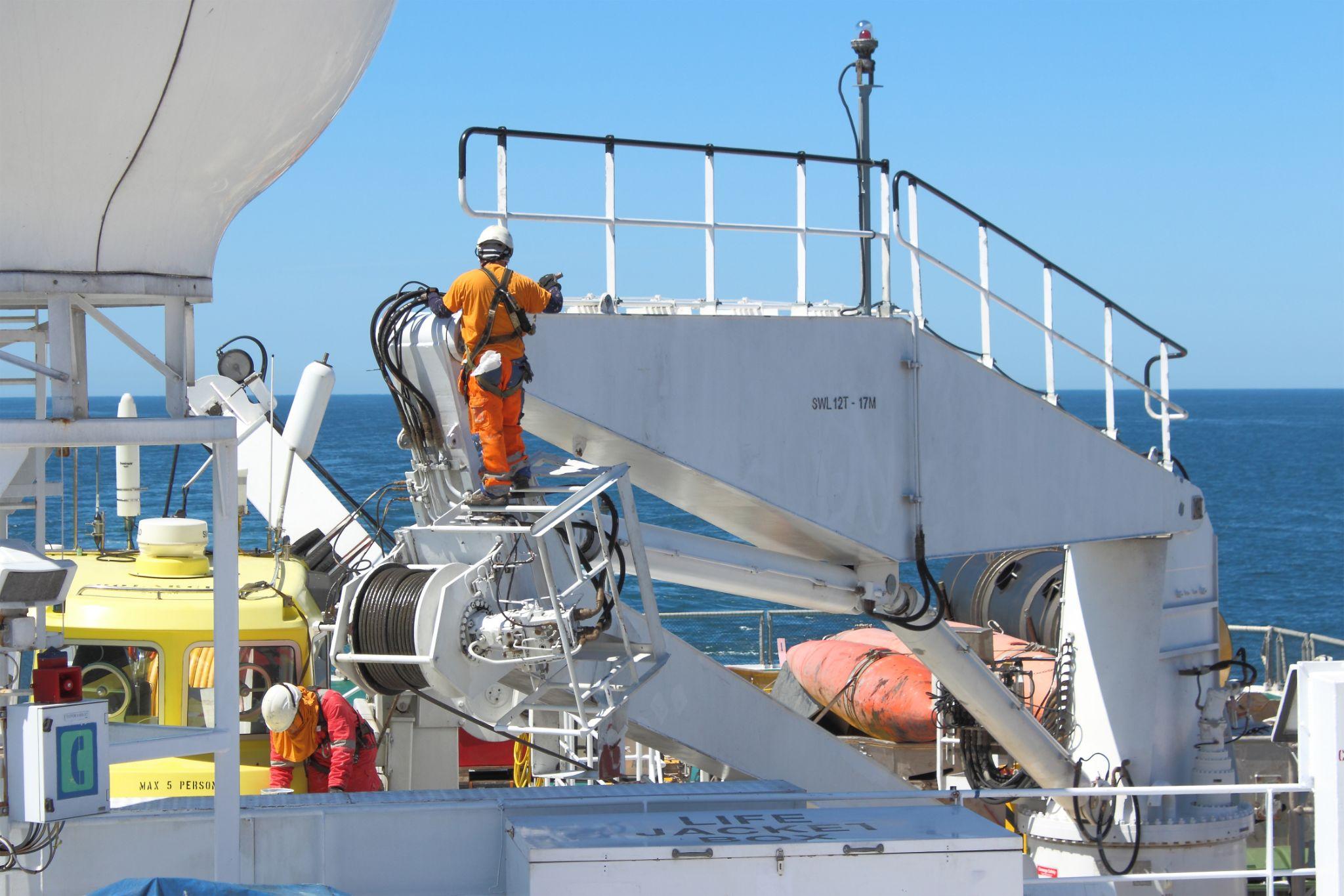 Seafarers painting ship's crane while out at sea