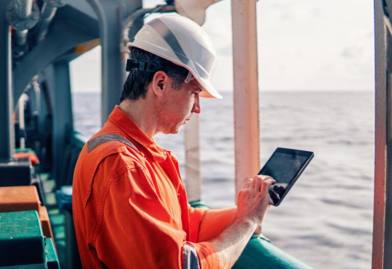 Marine captain on deck of vessel watching digital tablet.