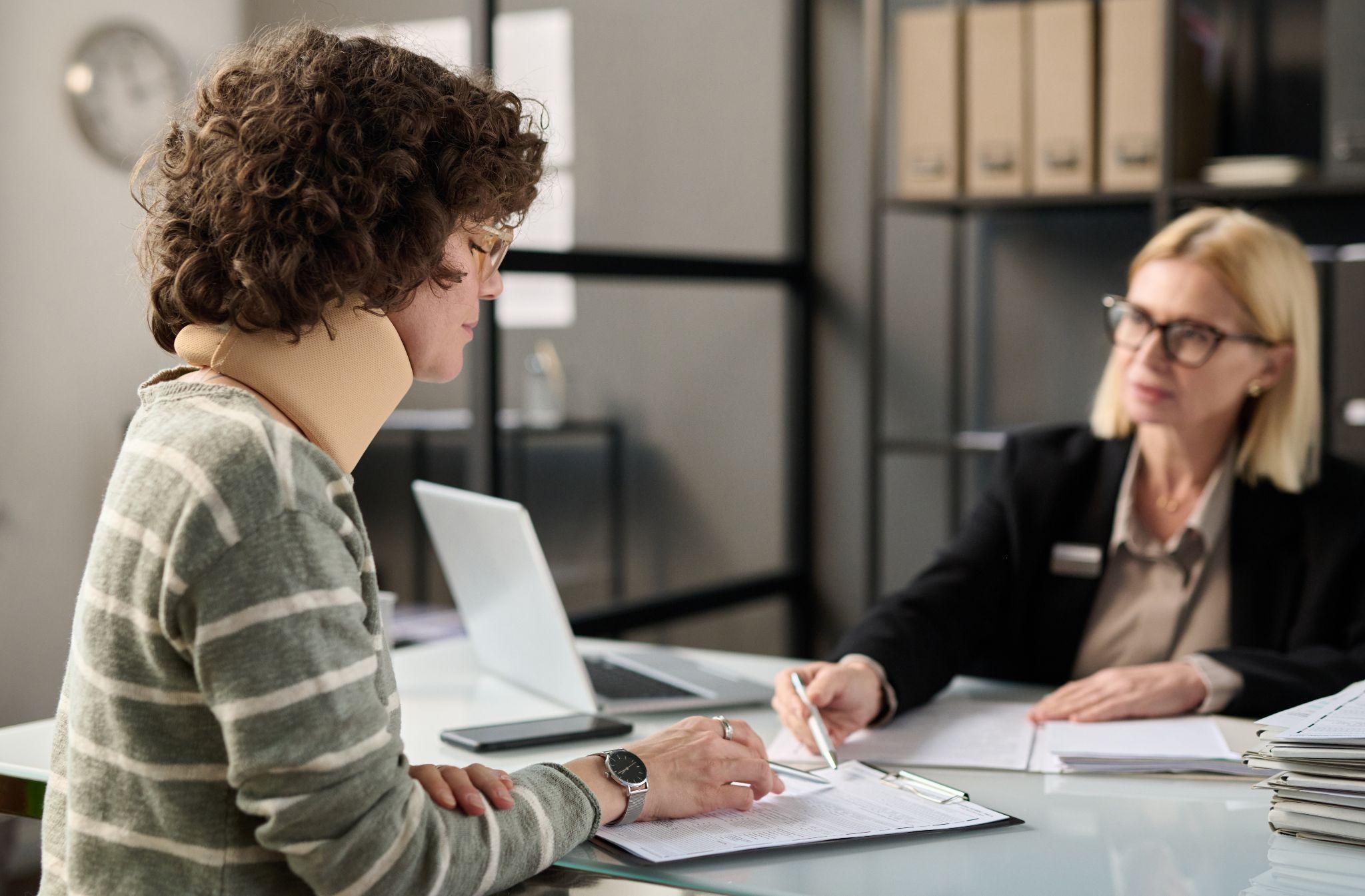 Side view portrait of young woman with neck injury filling documents at insurance agency office