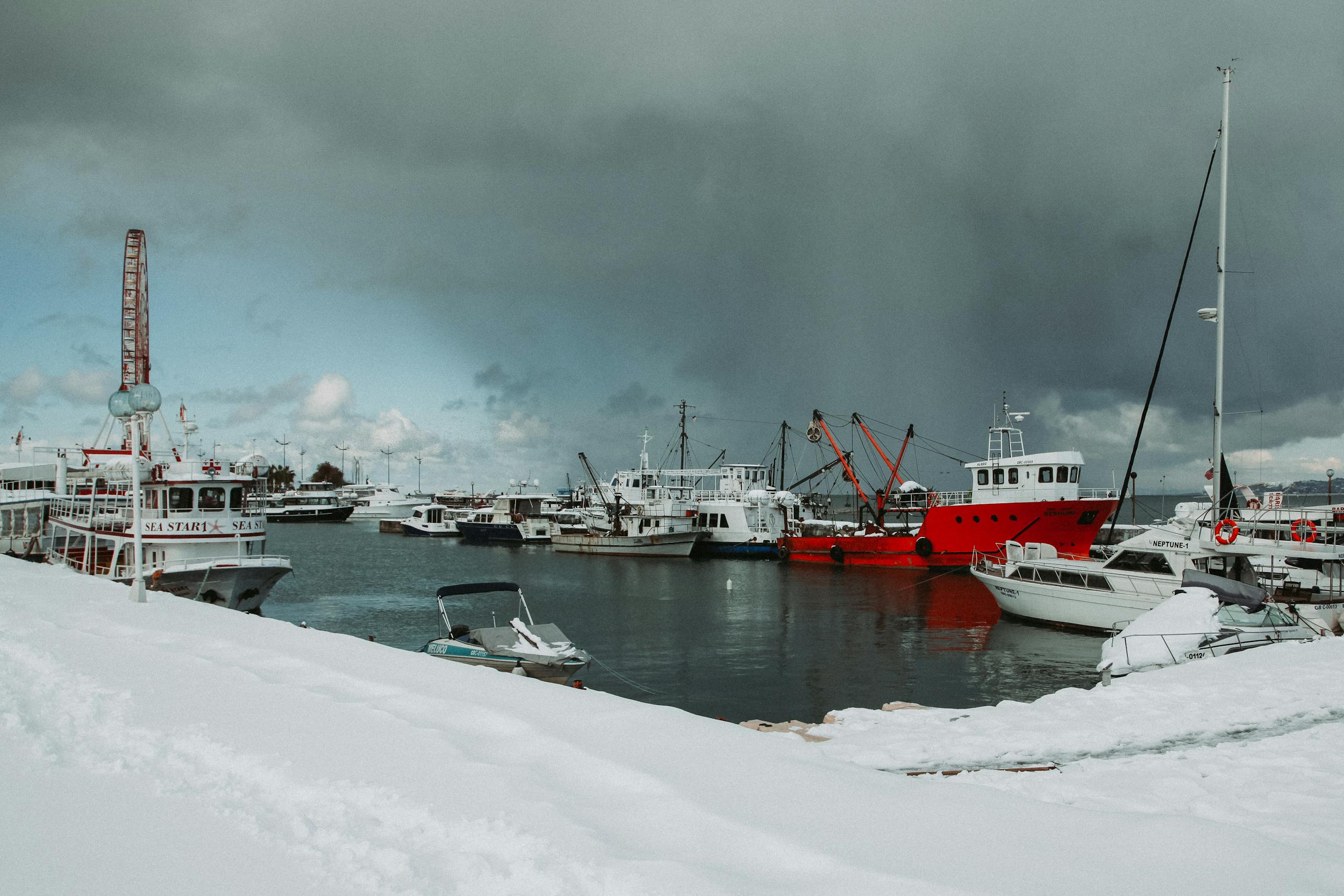 Seashore covered with snow near sea with various ships and yachts against overcast sky in port in cold winter day